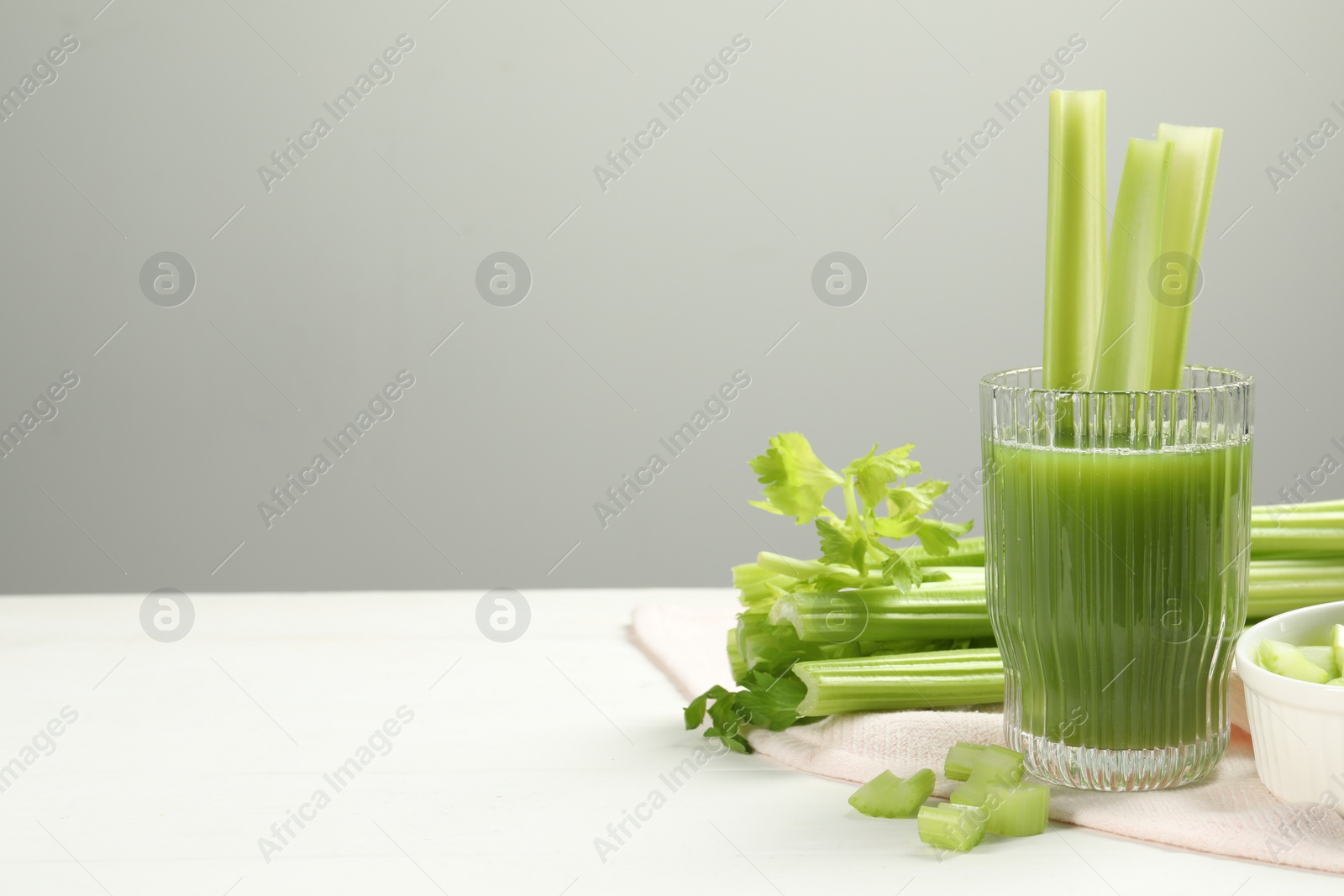 Photo of Glass of celery juice and fresh vegetables on white table, space for text