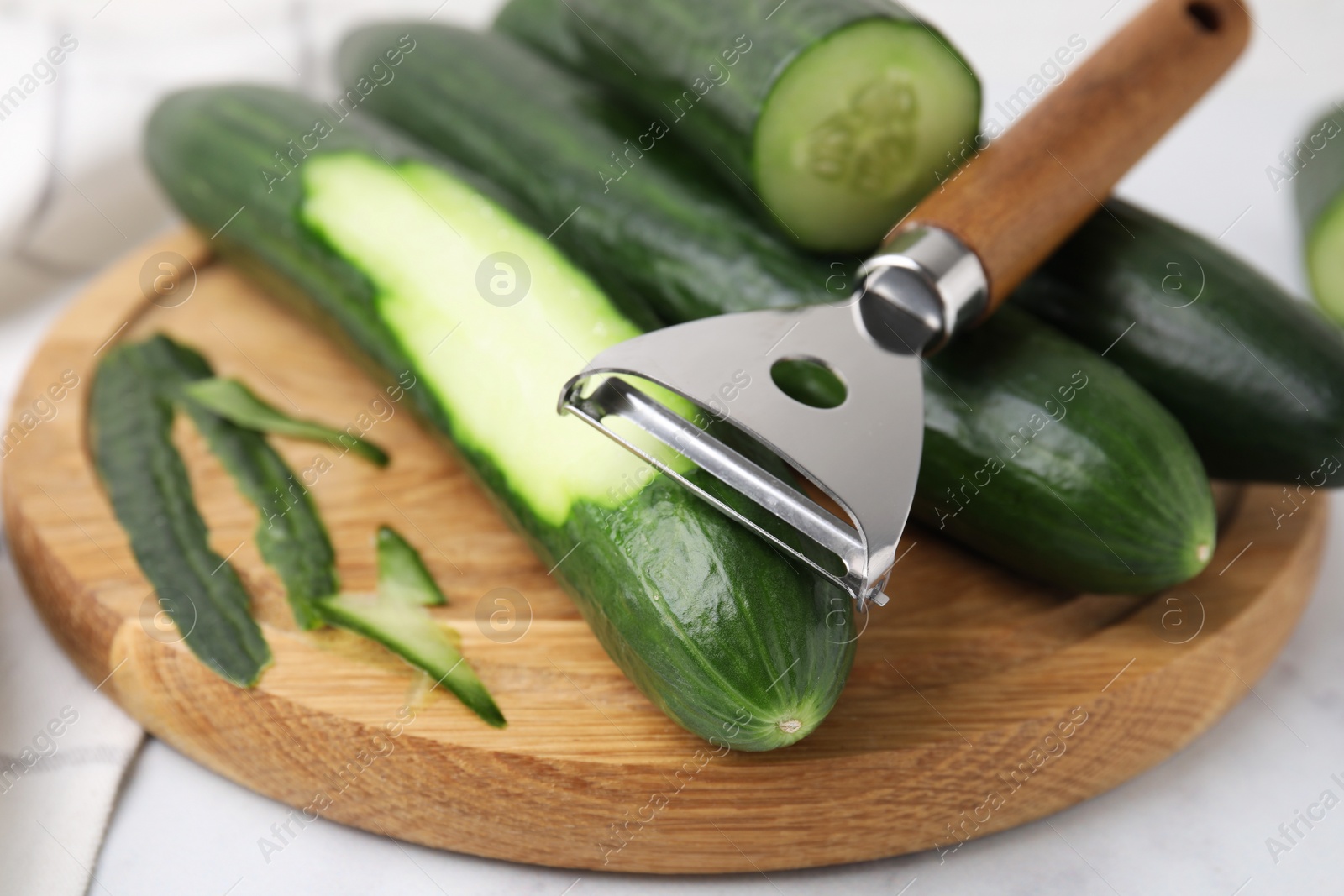 Photo of Fresh cucumbers and peeler on white table, closeup