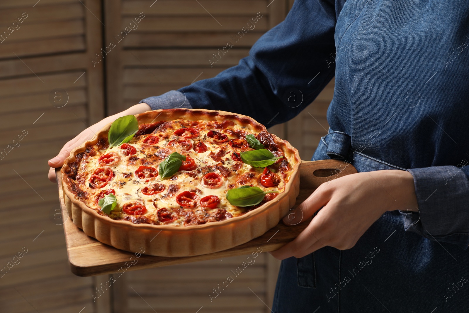 Photo of Woman holding delicious homemade quiche with prosciutto against wooden folding screen, closeup