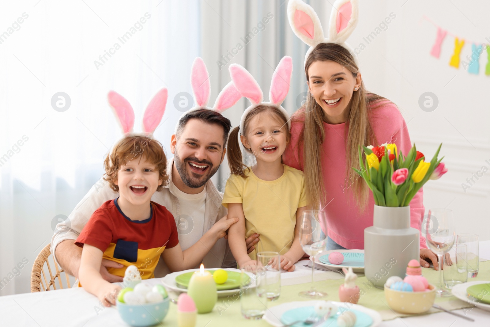 Photo of Easter celebration. Portrait of happy family with bunny ears at served table in room