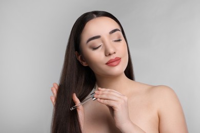 Photo of Young woman applying essential oil onto hair on light grey background