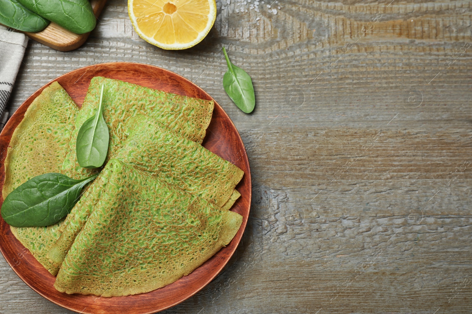 Photo of Delicious spinach crepes served on wooden table, flat lay. Space for text