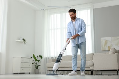 Happy man cleaning floor with steam mop at home. Space for text