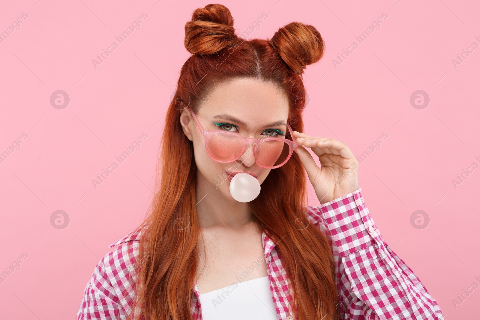 Photo of Beautiful woman with bright makeup blowing bubble gum on pink background