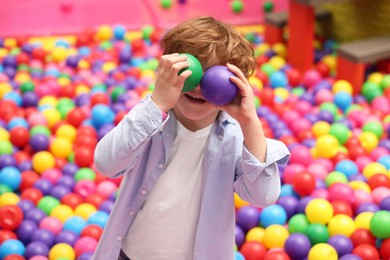 Photo of Happy little boy holding colorful balls in ball pit