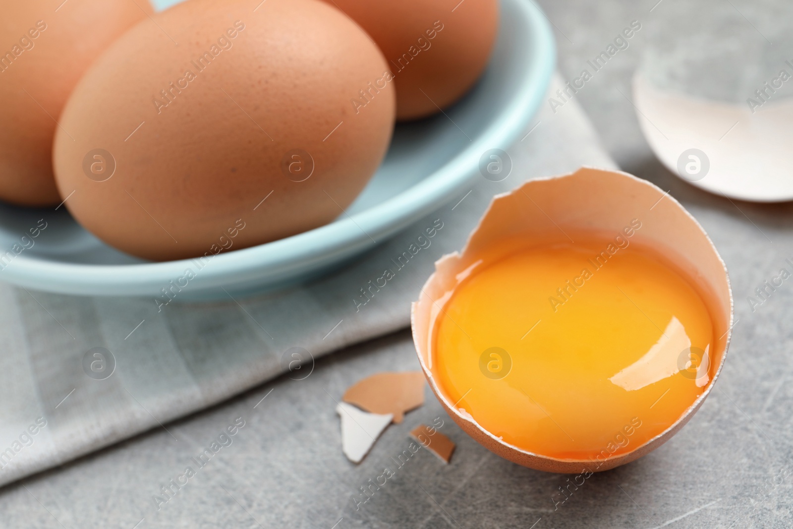 Photo of Raw chicken eggs and shell with yolk on light grey table, closeup