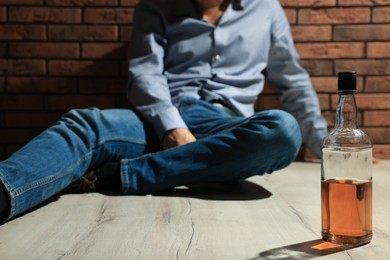 Photo of Addicted man sitting near red brick wall, focus on bottle of alcoholic drink