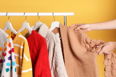 Woman choosing sweater on rack against color background