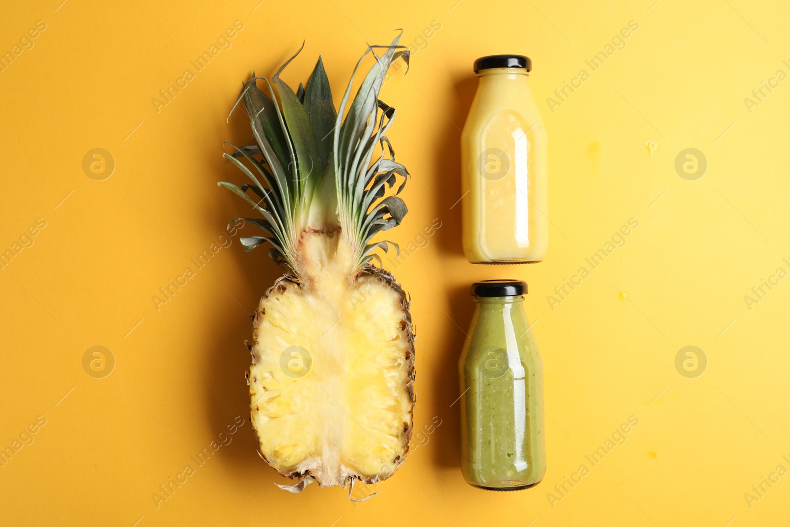 Photo of Bottles with delicious colorful juices and cut pineapple on yellow background, flat lay