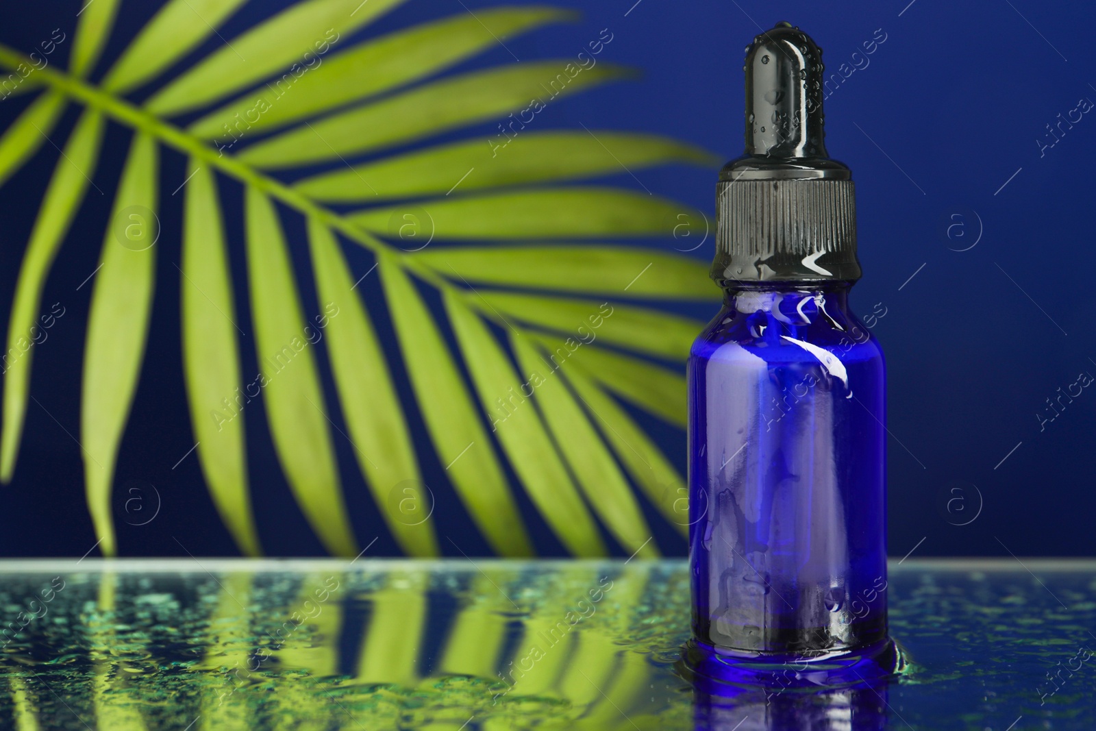 Photo of Bottle of face serum on wet surface against blue background, closeup. Space for text