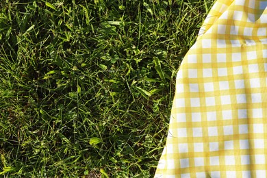 Photo of Checkered picnic tablecloth on fresh green grass, top view. Space for text