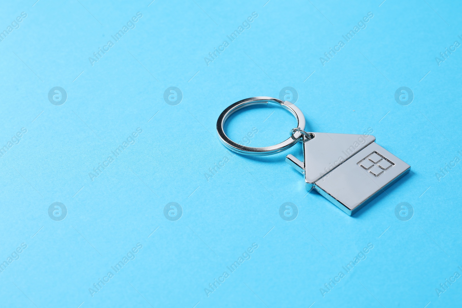 Photo of Metallic keychain in shape of house on light blue background. Space for text