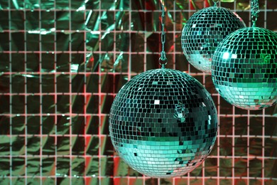 Shiny disco balls against foil party curtain under color lights, space for text