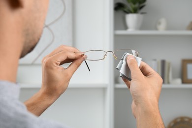 Photo of Man wiping glasses with microfiber cloth indoors, closeup