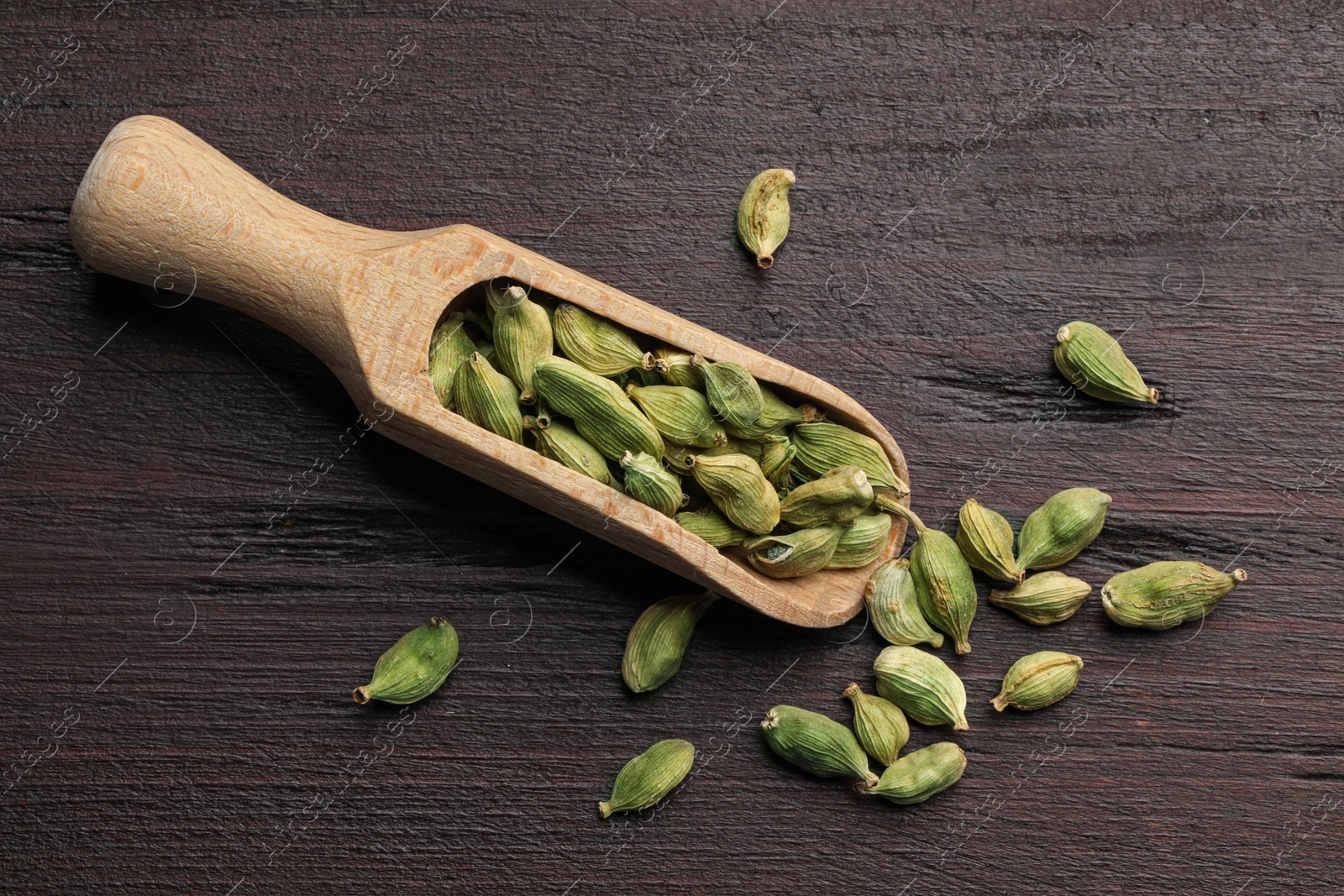 Photo of Scoop with dry cardamom pods on wooden table, top view