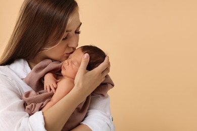 Mother kissing her cute newborn baby on beige background. Space for text