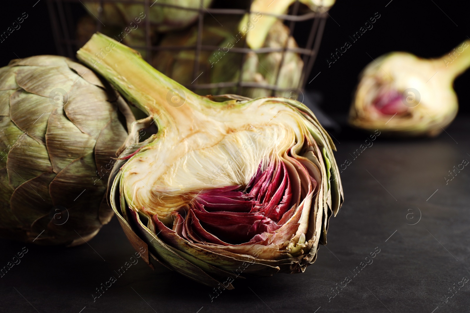 Photo of Cut and whole fresh raw artichokes on black table, closeup