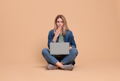 Emotional woman with laptop on beige background