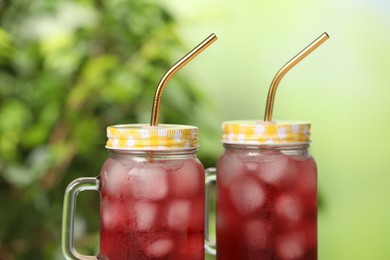 Refreshing hibiscus tea with ice cubes in mason jars against blurred green background