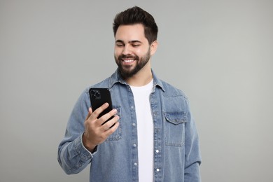 Photo of Happy young man using smartphone on grey background