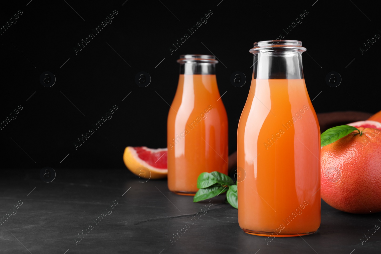 Photo of Tasty freshly made grapefruit juice and fruit on black table. Space for text