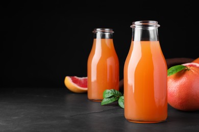 Photo of Tasty freshly made grapefruit juice and fruit on black table. Space for text