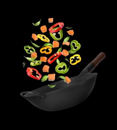 Image of Different tasty ingredients falling into wok on black background