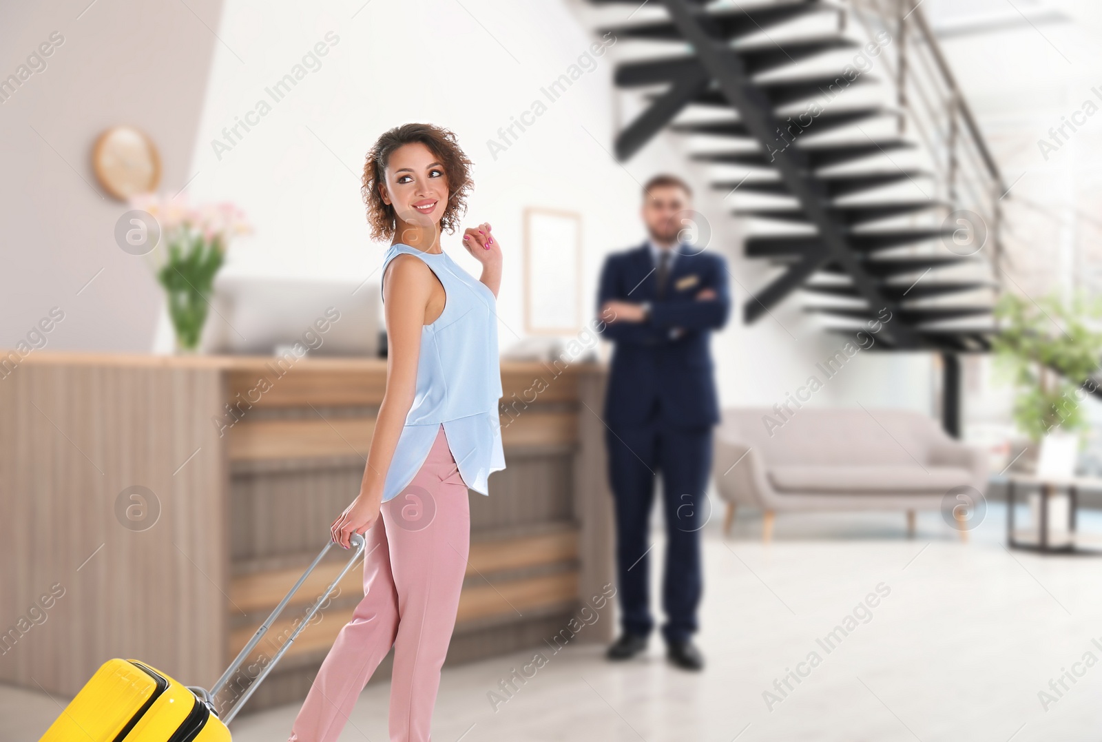 Image of Beautiful woman with suitcase near receptionist in hotel