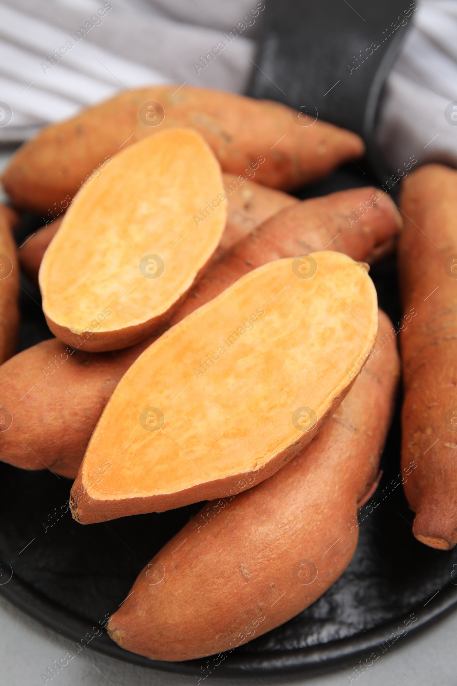 Photo of Slate board with cut and whole sweet potatoes on table, closeup