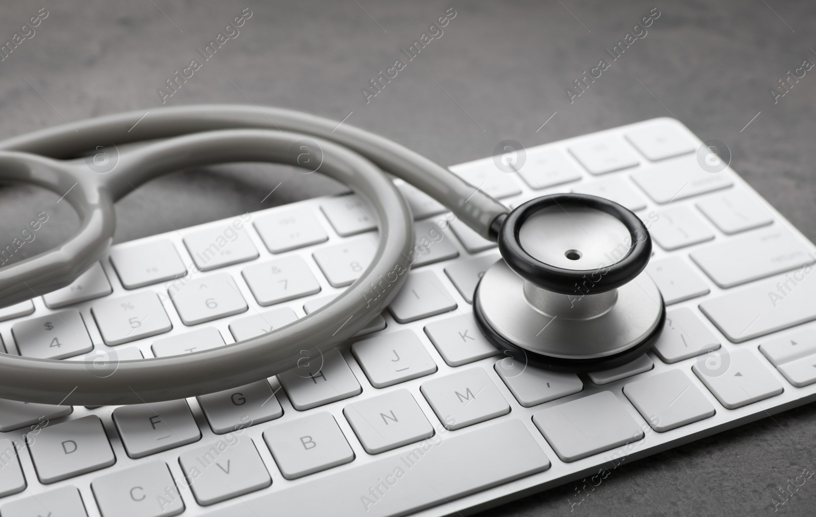 Photo of Computer keyboard with stethoscope on grey table, closeup