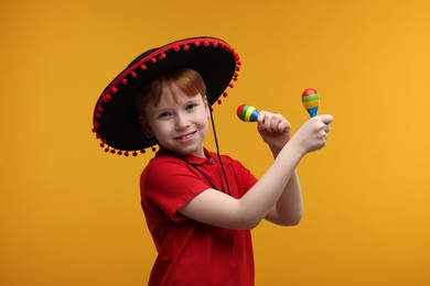 Photo of Cute boy in Mexican sombrero hat with maracas on yellow background