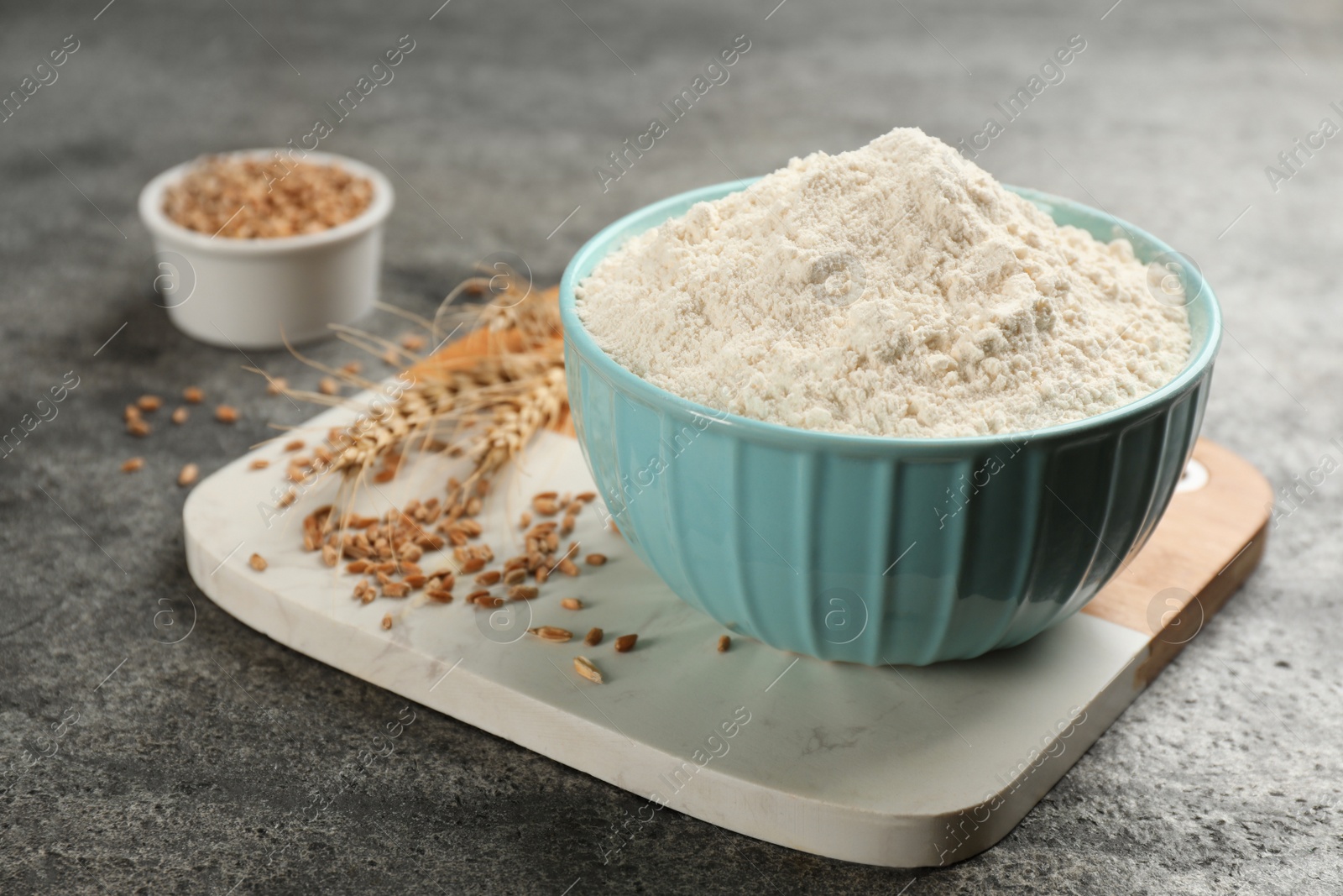Photo of Bowl of flour and wheat kernels on grey table