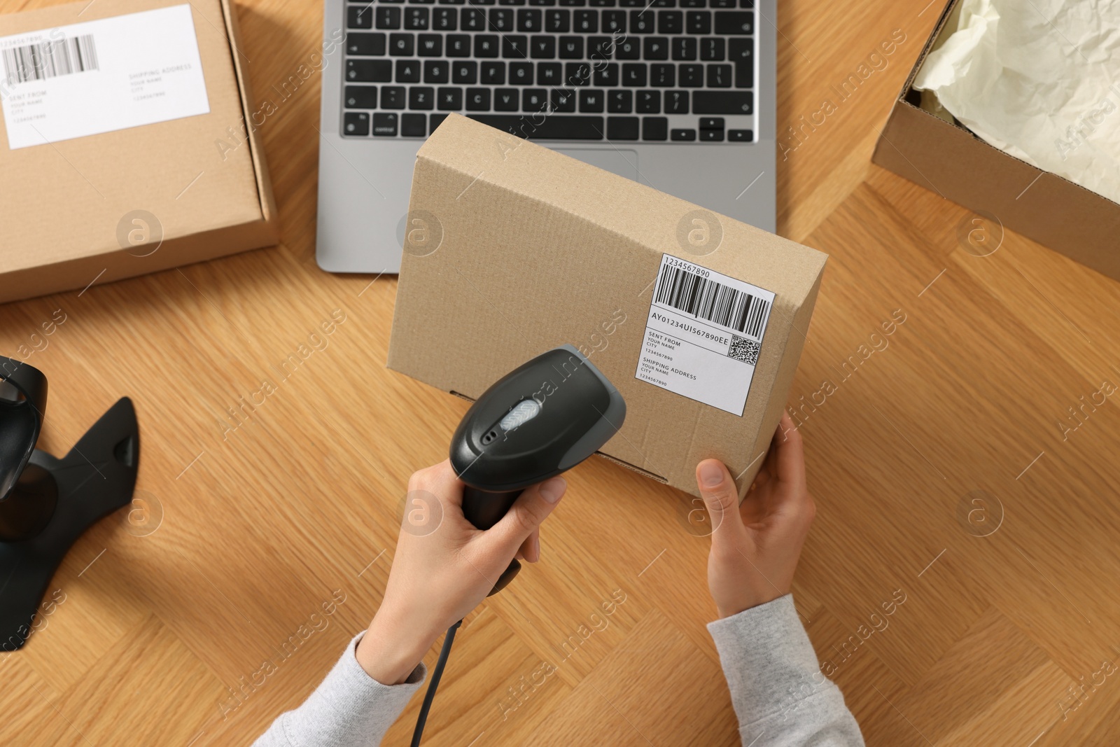 Photo of Woman with scanner reading parcel barcode at wooden table, top view. Online store