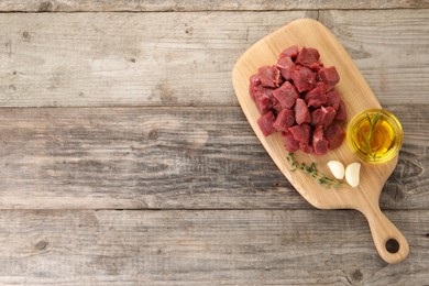 Photo of Pieces of raw beef meat, oil and garlic on wooden table, top view. Space for text