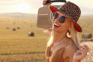 Happy hippie woman with radio receiver in field, space for text