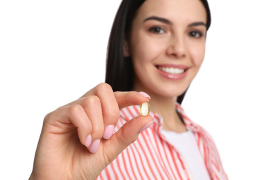 Young woman with vitamin capsule against white background, focus on hand