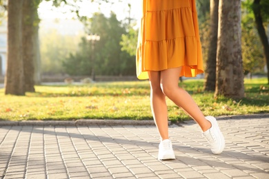 Photo of Woman wearing stylish yellow dress and sneakers in park, closeup