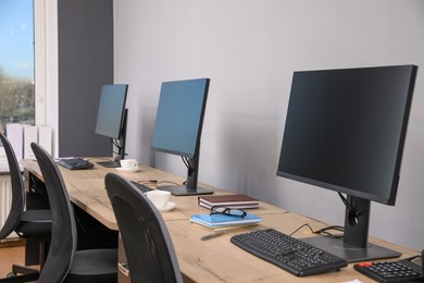 Photo of Open office interior. Modern workplaces with computers near light grey wall