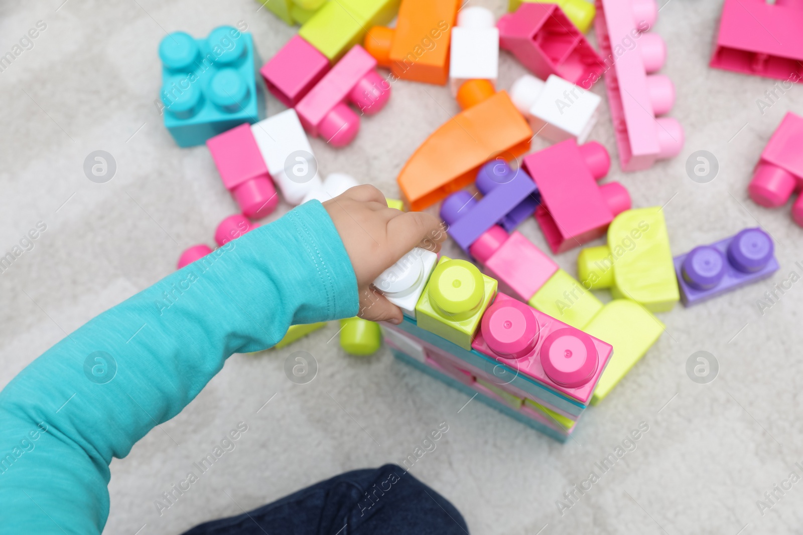 Photo of Top view of little child playing with building blocks on carpet, closeup