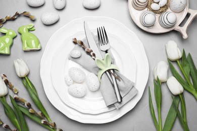 Festive table setting with painted eggs and tulips on light grey background, flat lay. Easter celebration