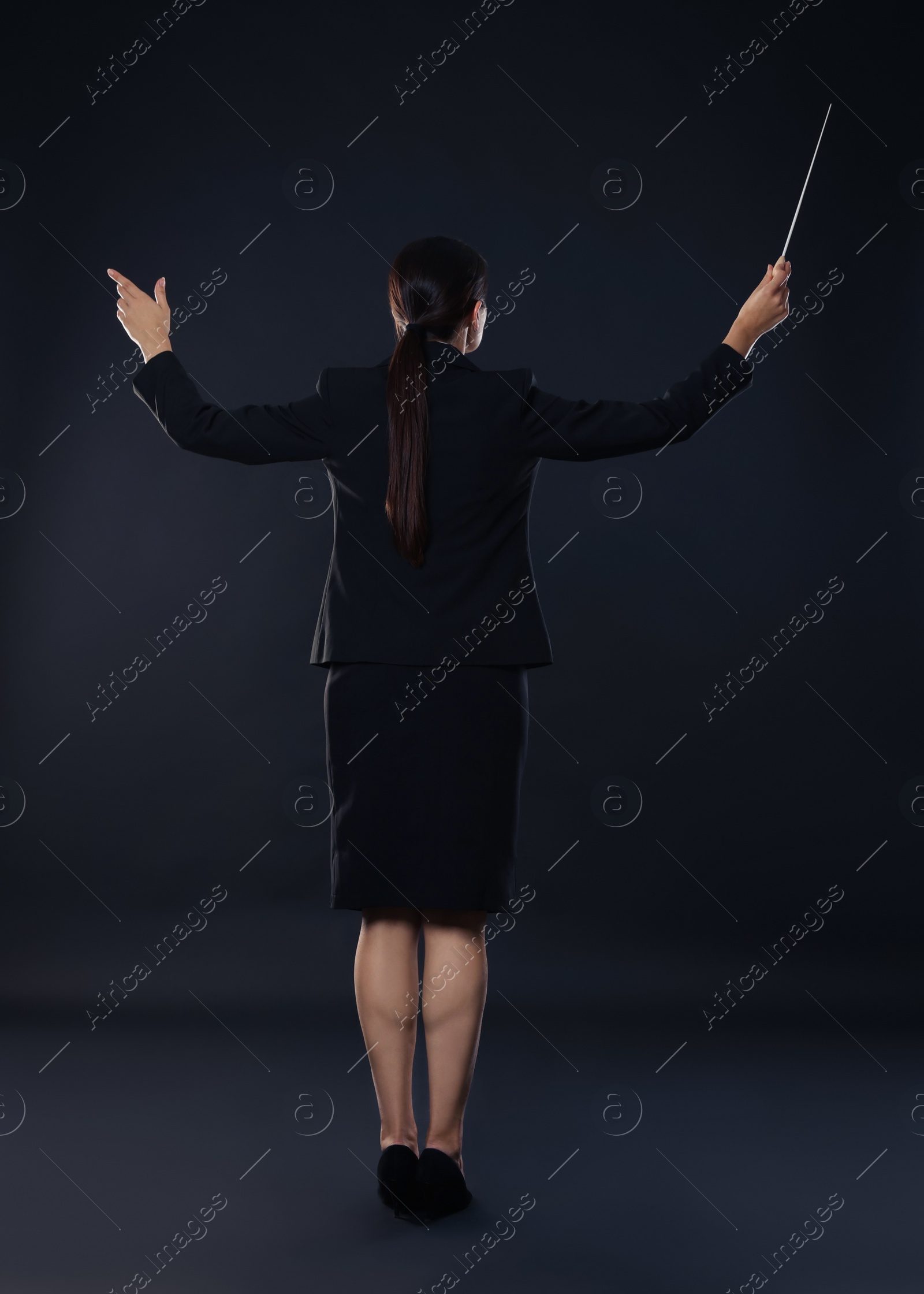 Photo of Professional conductor with baton on dark background, back view