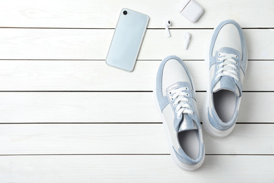 Pair of stylish shoes, modern smartphone and wireless earphones on white wooden table, flat lay. Space for text