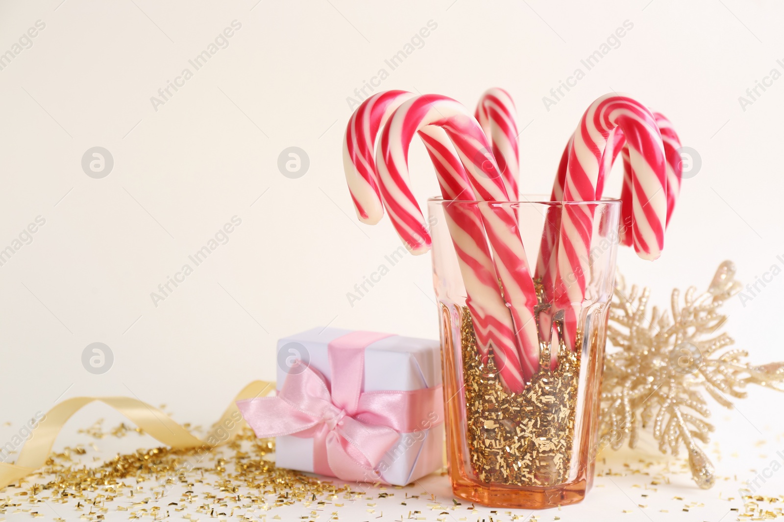 Photo of Christmas candy canes, gift box and confetti on beige background, space for text