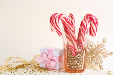 Photo of Christmas candy canes, gift box and confetti on beige background, space for text