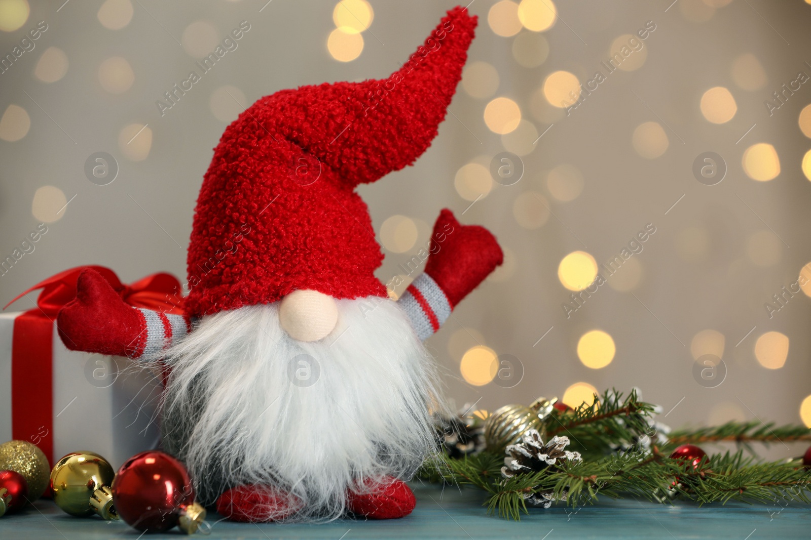 Photo of Cute Christmas gnome, gift box and festive decor on turquoise wooden table against blurred lights