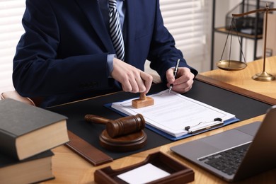 Photo of Notary with pen stamping document at wooden table in office, closeup