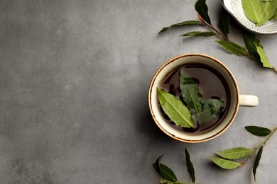 Photo of Cup of freshly brewed tea with bay leaves on grey table, flat lay. Space for text