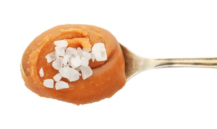 Spoon with delicious caramel and salt on white background