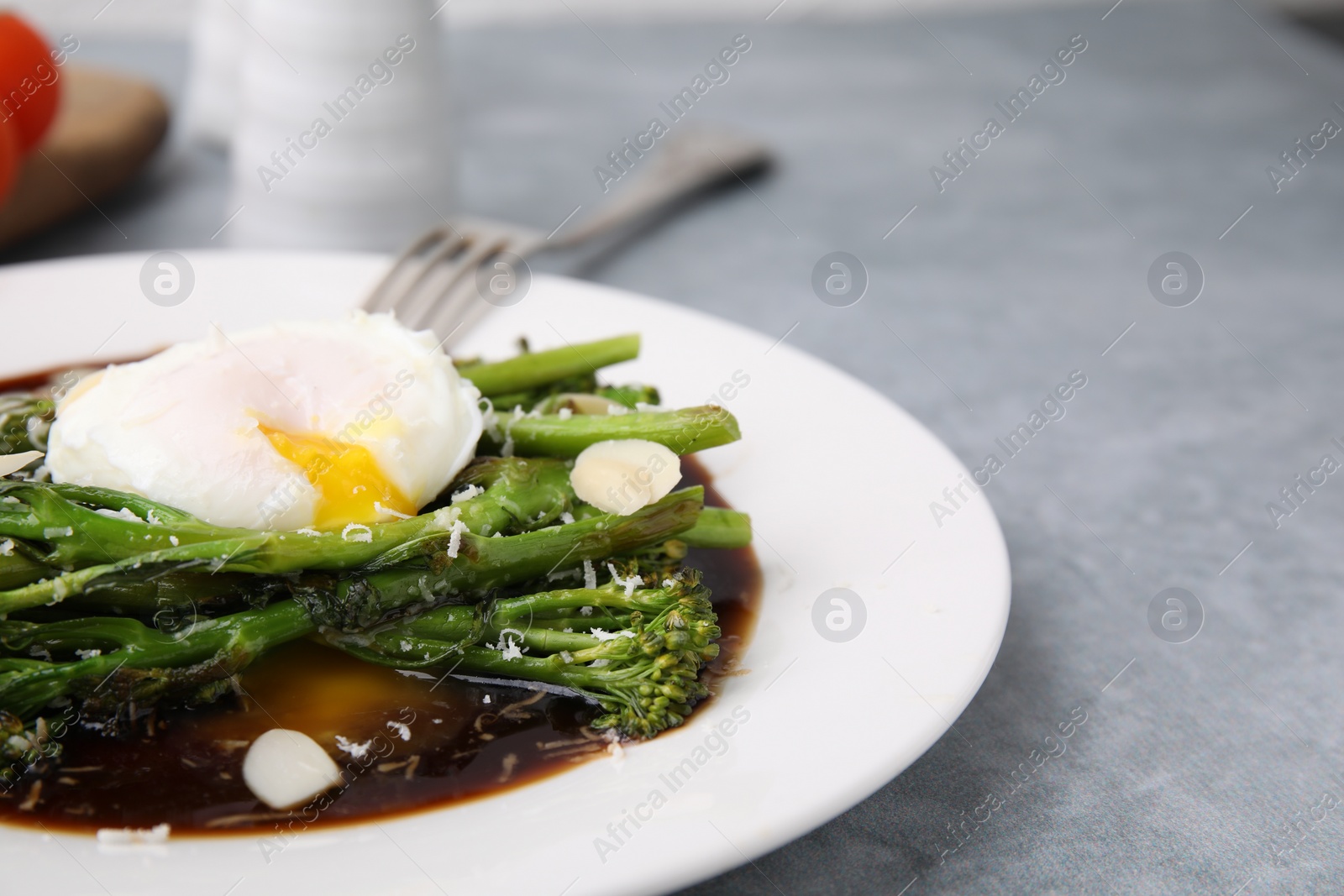 Photo of Tasty cooked broccolini with poached egg, almonds and sauce on grey table, closeup. Space for text