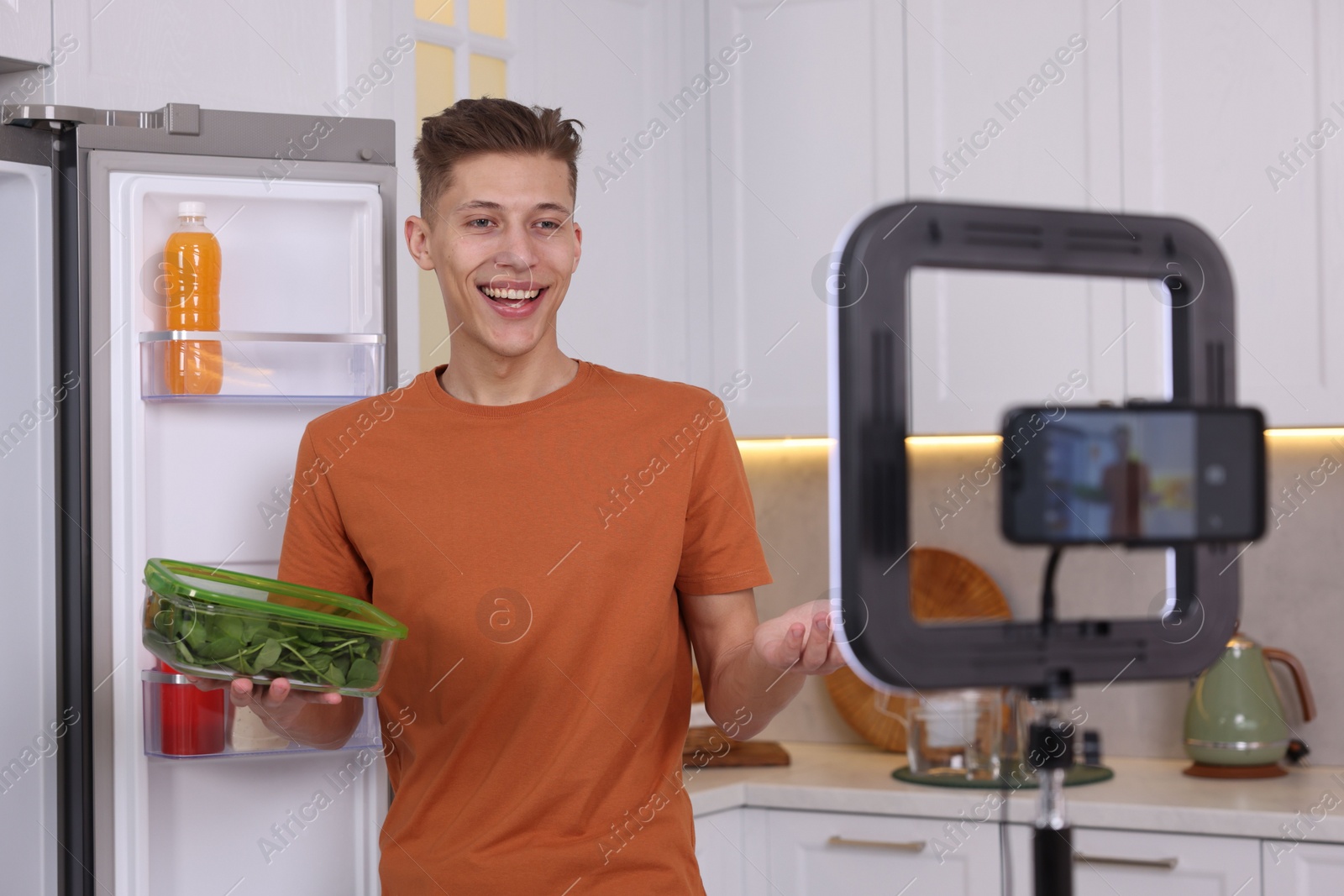 Photo of Smiling food blogger explaining something while recording video in kitchen